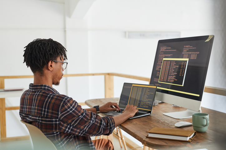 Computer programmer sitting at desk writing code on computer